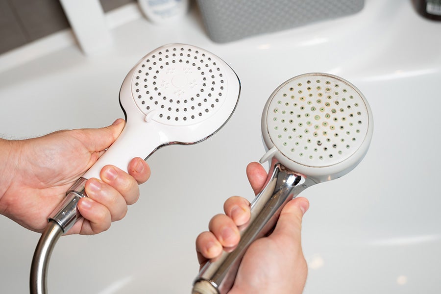 A person changing a shower head and holding the old and new shower heads.