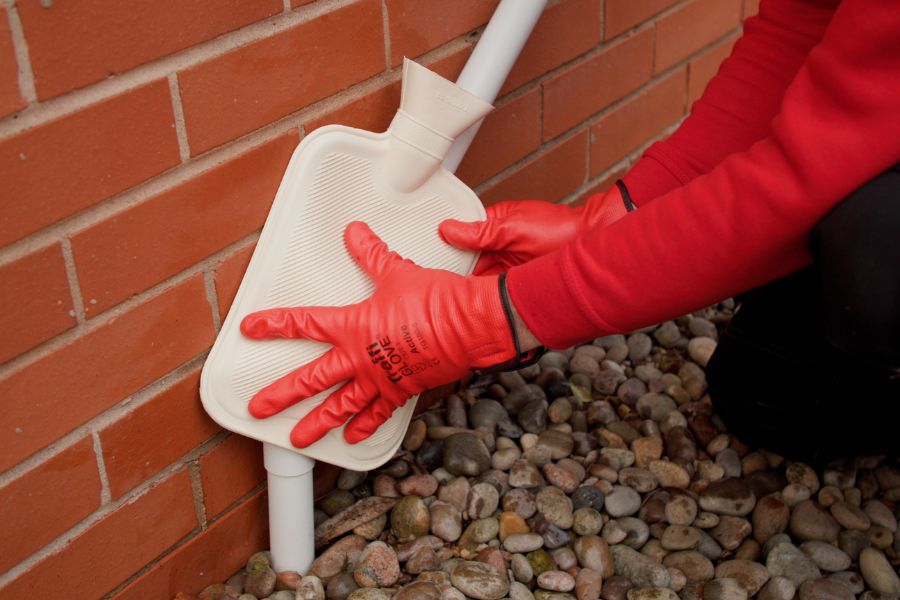 Image of a hot water bottle being used to thaw a frozen condensate pipe