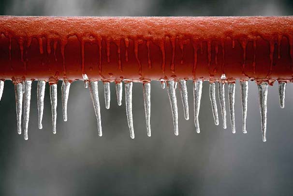 A frozen copper pipe with small icicles hanging from it 